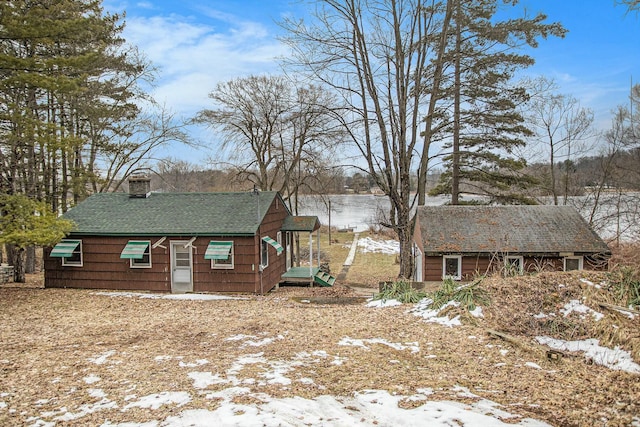 snow covered property featuring roof with shingles, an outdoor structure, and a chimney