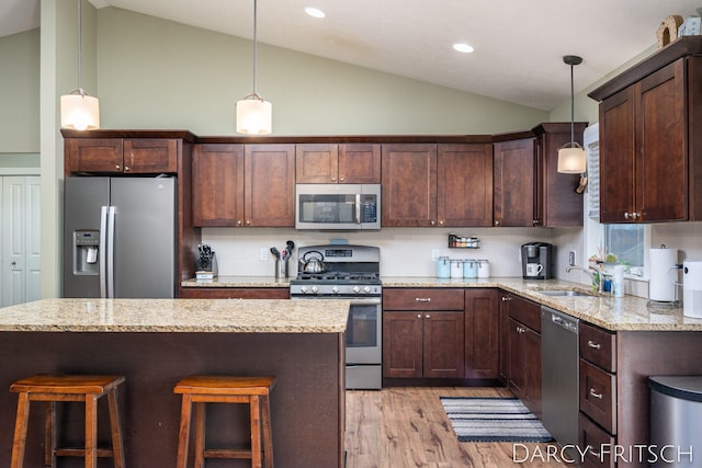 kitchen with a breakfast bar area, stainless steel appliances, dark brown cabinets, light wood-type flooring, and a sink