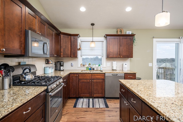 kitchen featuring light wood finished floors, appliances with stainless steel finishes, light stone counters, hanging light fixtures, and a sink