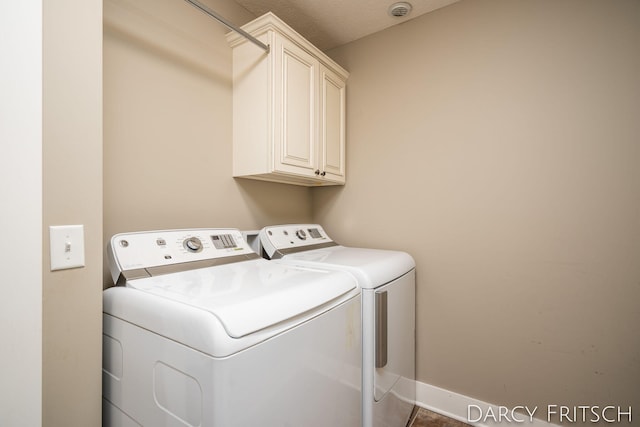 clothes washing area featuring separate washer and dryer, cabinet space, and baseboards