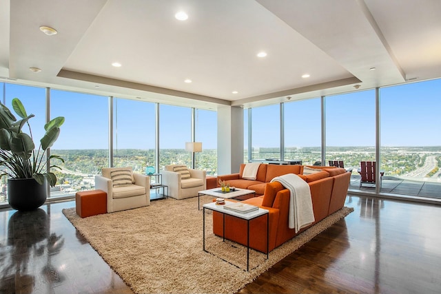 living room with a wealth of natural light, floor to ceiling windows, a raised ceiling, and wood finished floors