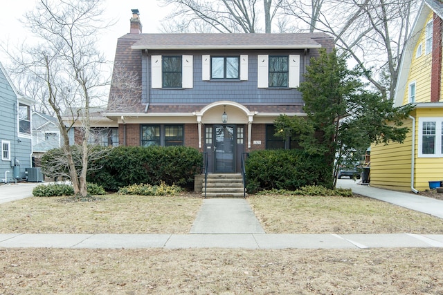 view of front of house with roof with shingles, brick siding, a chimney, and cooling unit