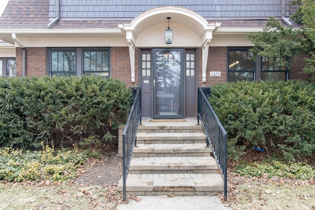 property entrance featuring brick siding, roof with shingles, and mansard roof