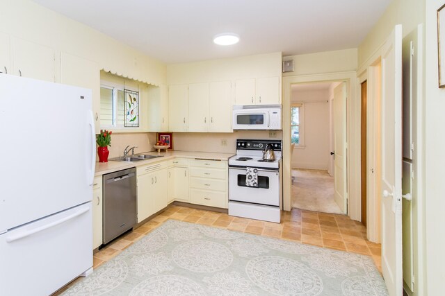 kitchen with white appliances, a sink, white cabinetry, light countertops, and a wealth of natural light