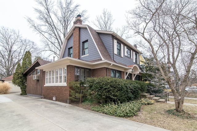 view of side of home featuring brick siding, a chimney, a shingled roof, and a gambrel roof