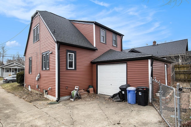 view of side of home with a shingled roof, concrete driveway, an attached garage, a gate, and fence