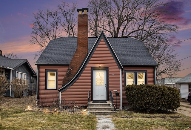 view of front facade with roof with shingles and a chimney