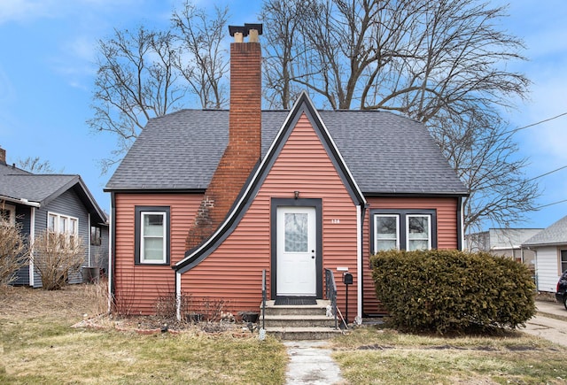 bungalow with roof with shingles, a chimney, and a front lawn