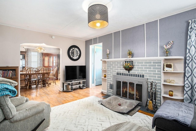 living room with crown molding, a fireplace, arched walkways, and wood finished floors