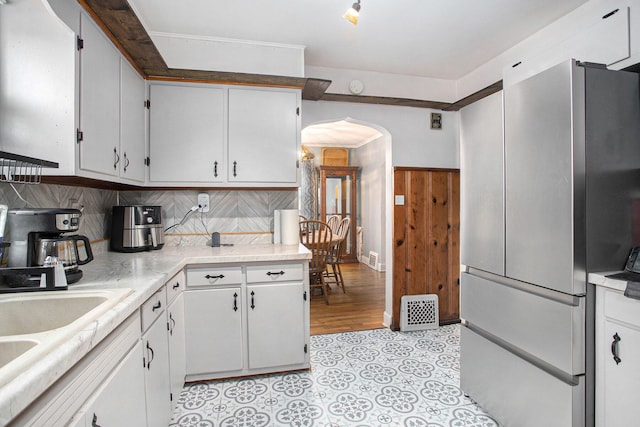 kitchen featuring arched walkways, white cabinetry, light countertops, freestanding refrigerator, and decorative backsplash