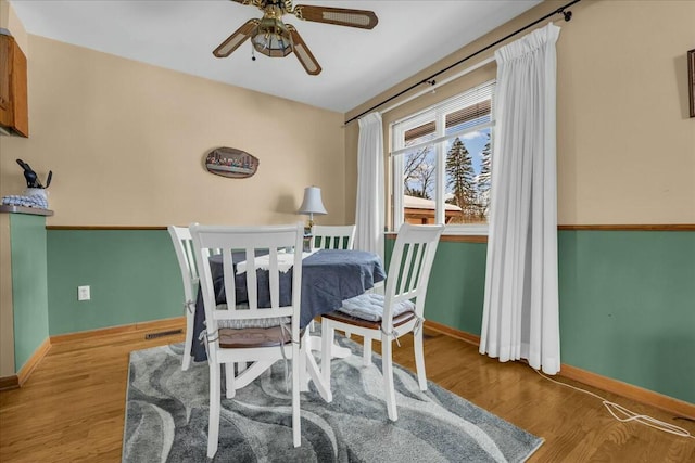 dining area featuring a ceiling fan, visible vents, baseboards, and wood finished floors