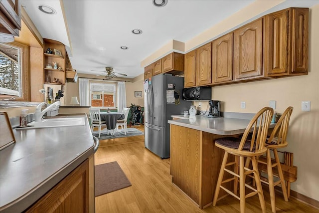 kitchen with light wood-style flooring, brown cabinetry, freestanding refrigerator, a sink, and a peninsula