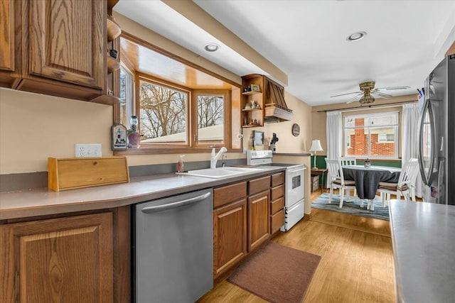 kitchen featuring brown cabinetry, stainless steel appliances, light wood-type flooring, premium range hood, and a sink