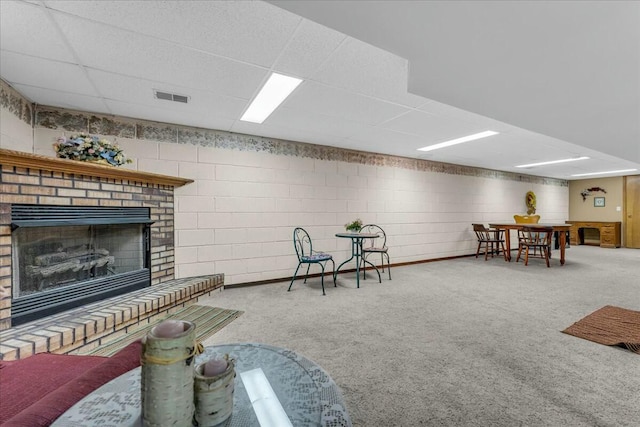 living room with concrete block wall, a brick fireplace, visible vents, and carpet floors