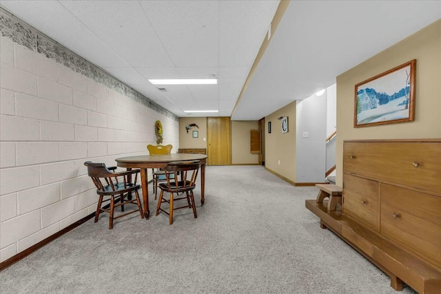 carpeted dining room with concrete block wall, baseboards, and stairway