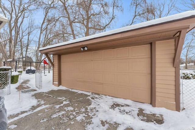 snow covered garage with a detached garage, fence, and a gate