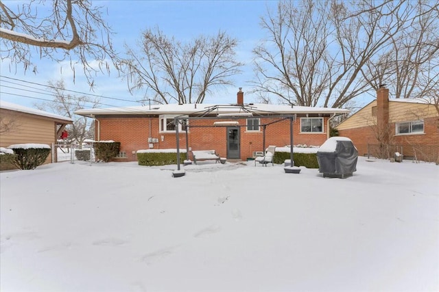 snow covered rear of property featuring brick siding and a chimney