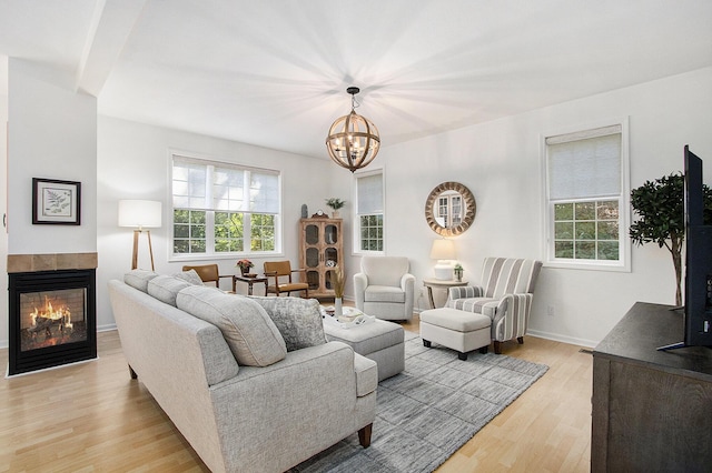 living room with light wood finished floors, a notable chandelier, baseboards, and a tiled fireplace