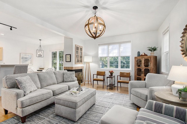 living area featuring an inviting chandelier, a glass covered fireplace, a wealth of natural light, and wood finished floors