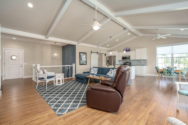 living room featuring lofted ceiling with beams, a barn door, light wood finished floors, and ceiling fan with notable chandelier