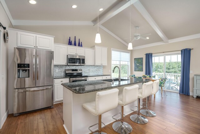 kitchen featuring dark wood finished floors, vaulted ceiling with beams, stainless steel appliances, backsplash, and a sink