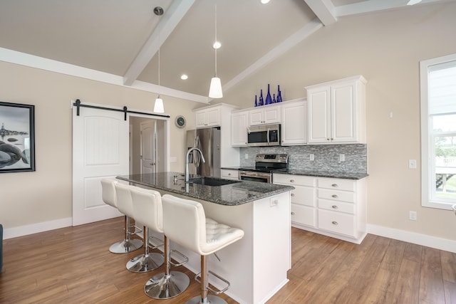 kitchen with backsplash, a barn door, appliances with stainless steel finishes, a sink, and beamed ceiling