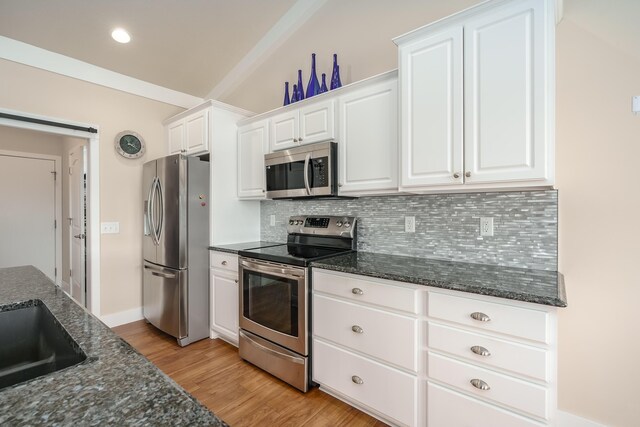 kitchen with stainless steel appliances, tasteful backsplash, light wood-style flooring, white cabinets, and dark stone countertops