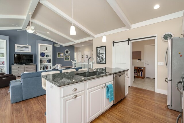 kitchen featuring lofted ceiling with beams, a barn door, appliances with stainless steel finishes, open floor plan, and a sink