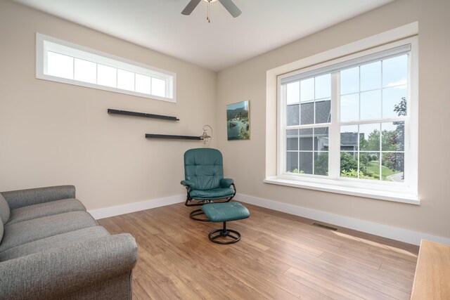 sitting room with a ceiling fan, visible vents, baseboards, and wood finished floors