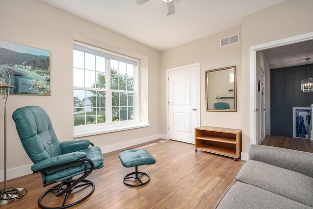 sitting room featuring ceiling fan with notable chandelier, visible vents, baseboards, and wood finished floors