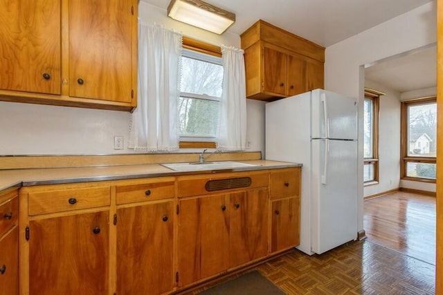 kitchen featuring brown cabinets, light countertops, a sink, and freestanding refrigerator