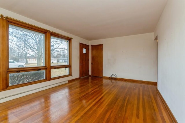 unfurnished room with a baseboard heating unit, baseboards, and wood finished floors