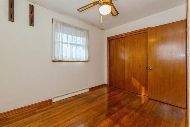 unfurnished bedroom with a baseboard heating unit, a closet, wood finished floors, and a ceiling fan