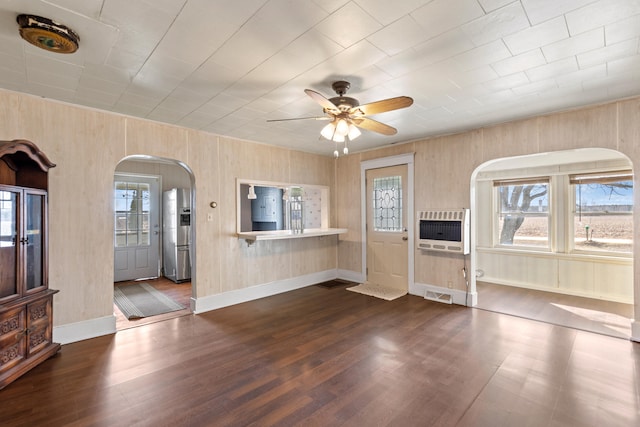 unfurnished living room with arched walkways, dark wood-style flooring, heating unit, visible vents, and a ceiling fan