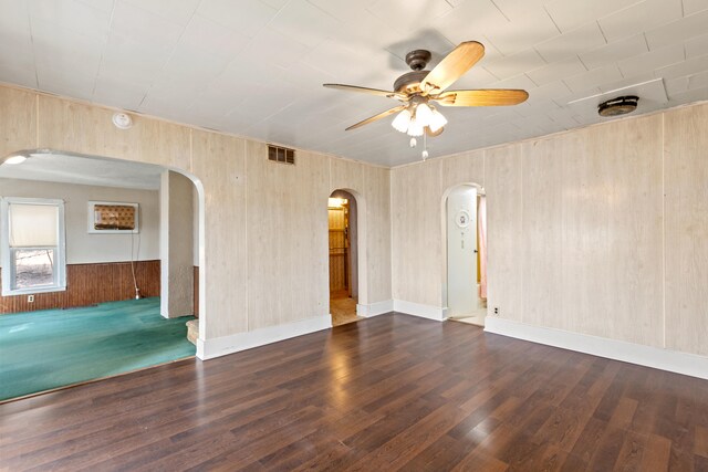 spare room featuring arched walkways, wood walls, wood finished floors, visible vents, and a ceiling fan