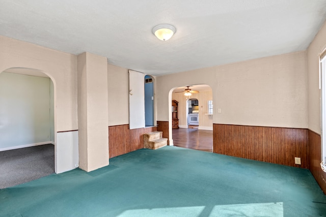 empty room featuring arched walkways, wainscoting, and wooden walls