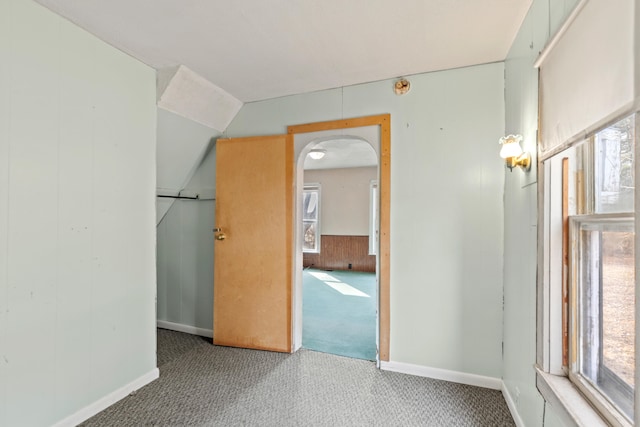 unfurnished room featuring wood walls, arched walkways, and carpet flooring