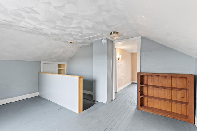 additional living space featuring a textured ceiling, wood-type flooring, lofted ceiling, and baseboards