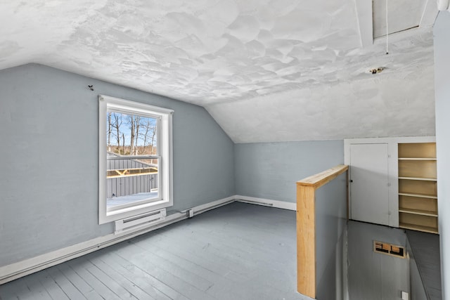 additional living space featuring lofted ceiling, hardwood / wood-style floors, attic access, a textured ceiling, and baseboards