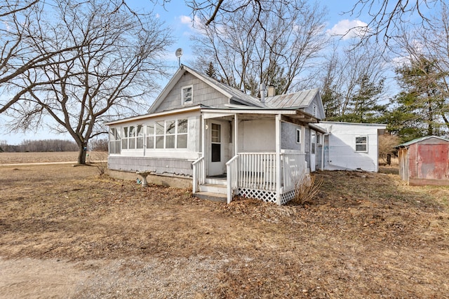 view of front of house with a storage shed, a chimney, a sunroom, and an outbuilding