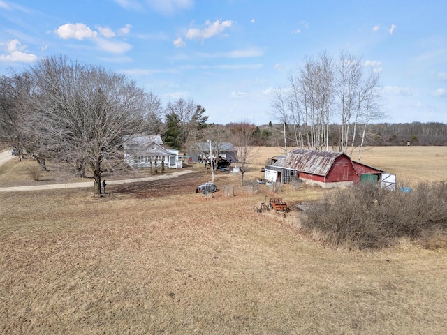 view of yard featuring a barn, driveway, a rural view, and an outbuilding