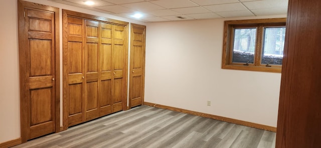 unfurnished bedroom featuring light wood-style floors, a paneled ceiling, a closet, and baseboards