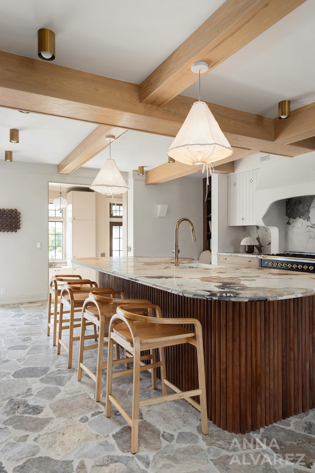 727 Plymouth Rd SE, East Grand Rapids, MI 49506 - kitchen with light stone finish flooring, beamed ceiling, a kitchen breakfast bar, white cabinetry, and decorative light fixtures