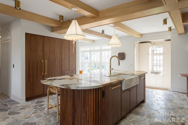 727 Plymouth Rd SE, East Grand Rapids, MI 49506 - kitchen featuring stone floors, beam ceiling, an island with sink, and pendant lighting