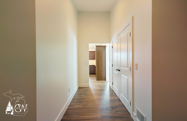 corridor with baseboards, a high ceiling, visible vents, and dark wood-type flooring