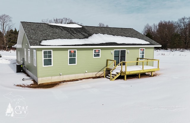 snow covered house featuring roof with shingles and a deck