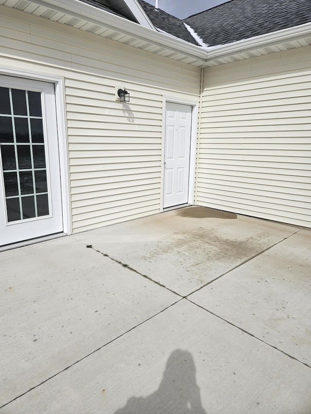 entrance to property with a shingled roof and a patio