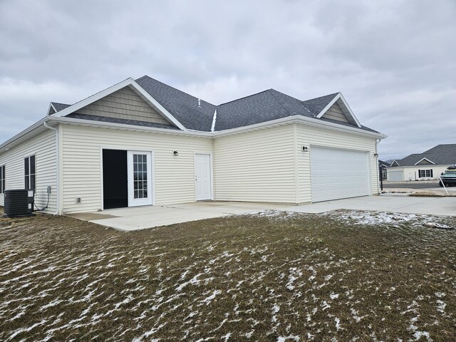 back of house with central air condition unit, a garage, driveway, roof with shingles, and a patio area