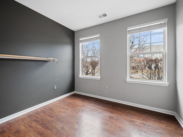 spare room featuring wood finished floors, visible vents, and baseboards