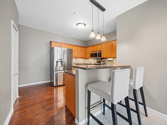 kitchen with a breakfast bar, dark wood-type flooring, decorative light fixtures, stainless steel appliances, and backsplash